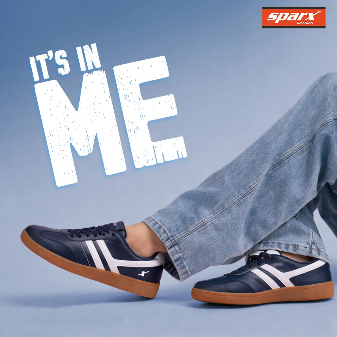 A person wearing navy Sparx sneakers with white side stripes and gum soles, paired with light blue jeans, against a blue studio background with large white text reading 'IT'S IN ME' and a Sparx logo in the top right.